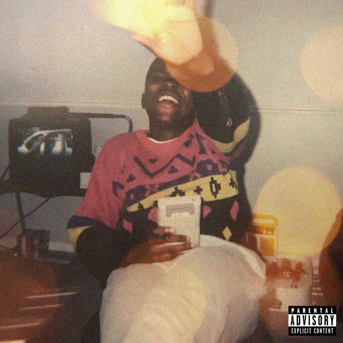 image is a photograph of a young man seated and smiling with one arm outstretched and the other holding a gameboy
