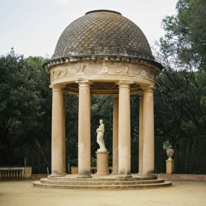 image is a photograph of a stone gazebo with a statue of a person in the middle